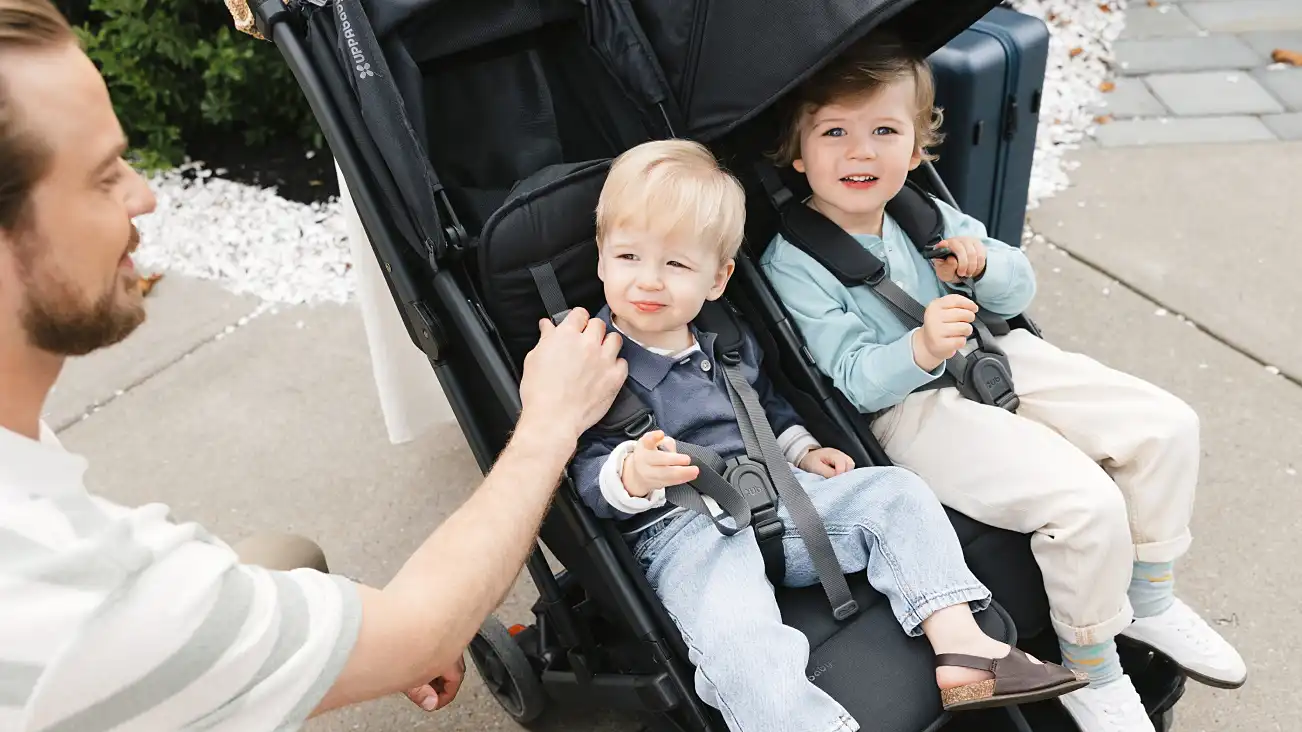 Two children of different sizes secured in the stroller seats
